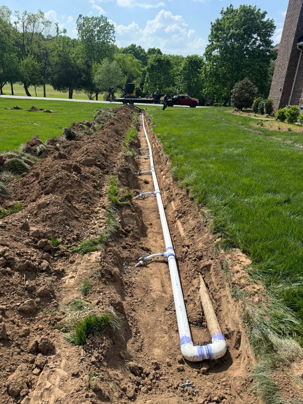 White PVC pipe laid in a narrow trench across a lawn