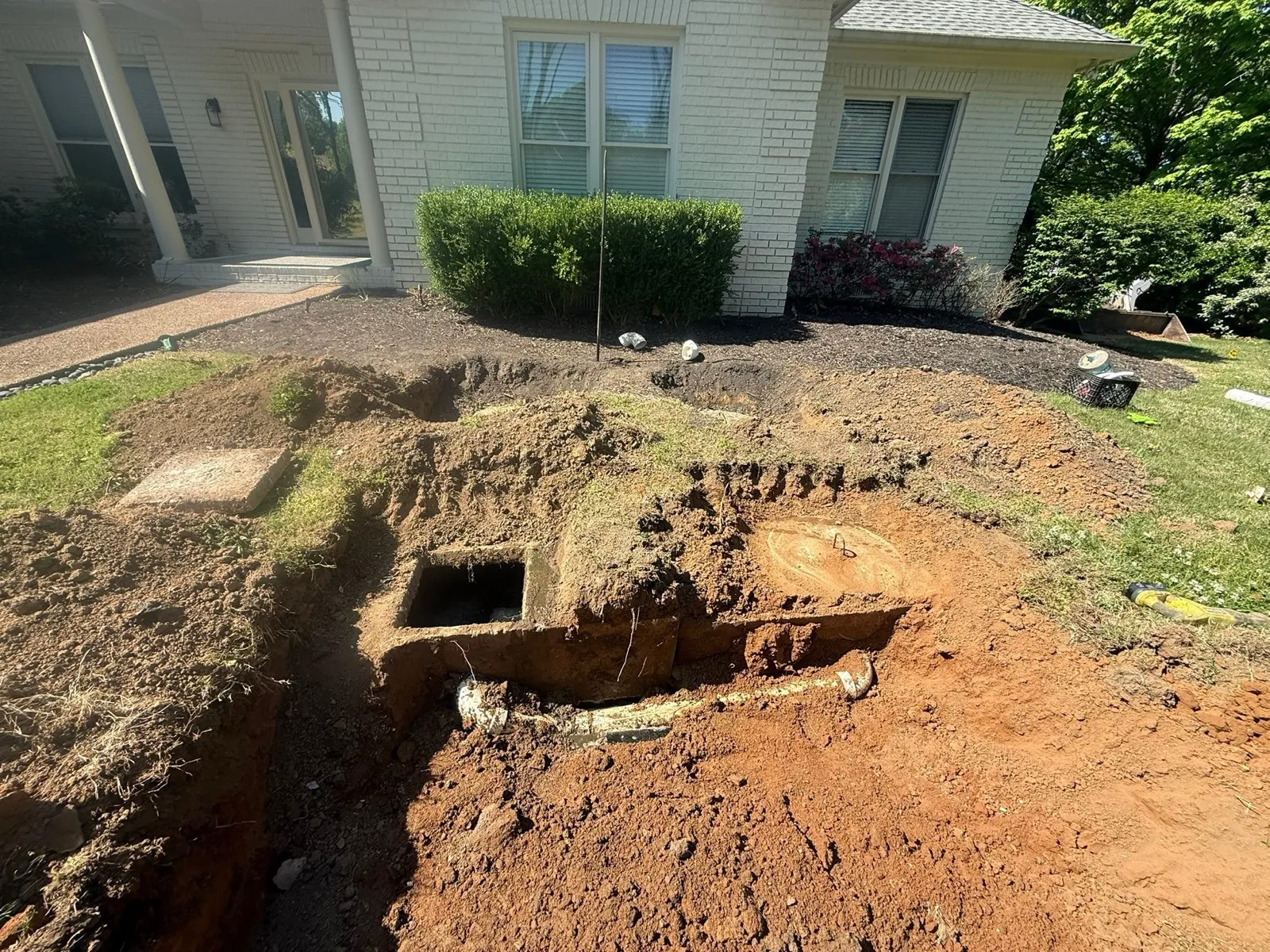 Buried septic tank dug out and opened in the yard beside a brick house