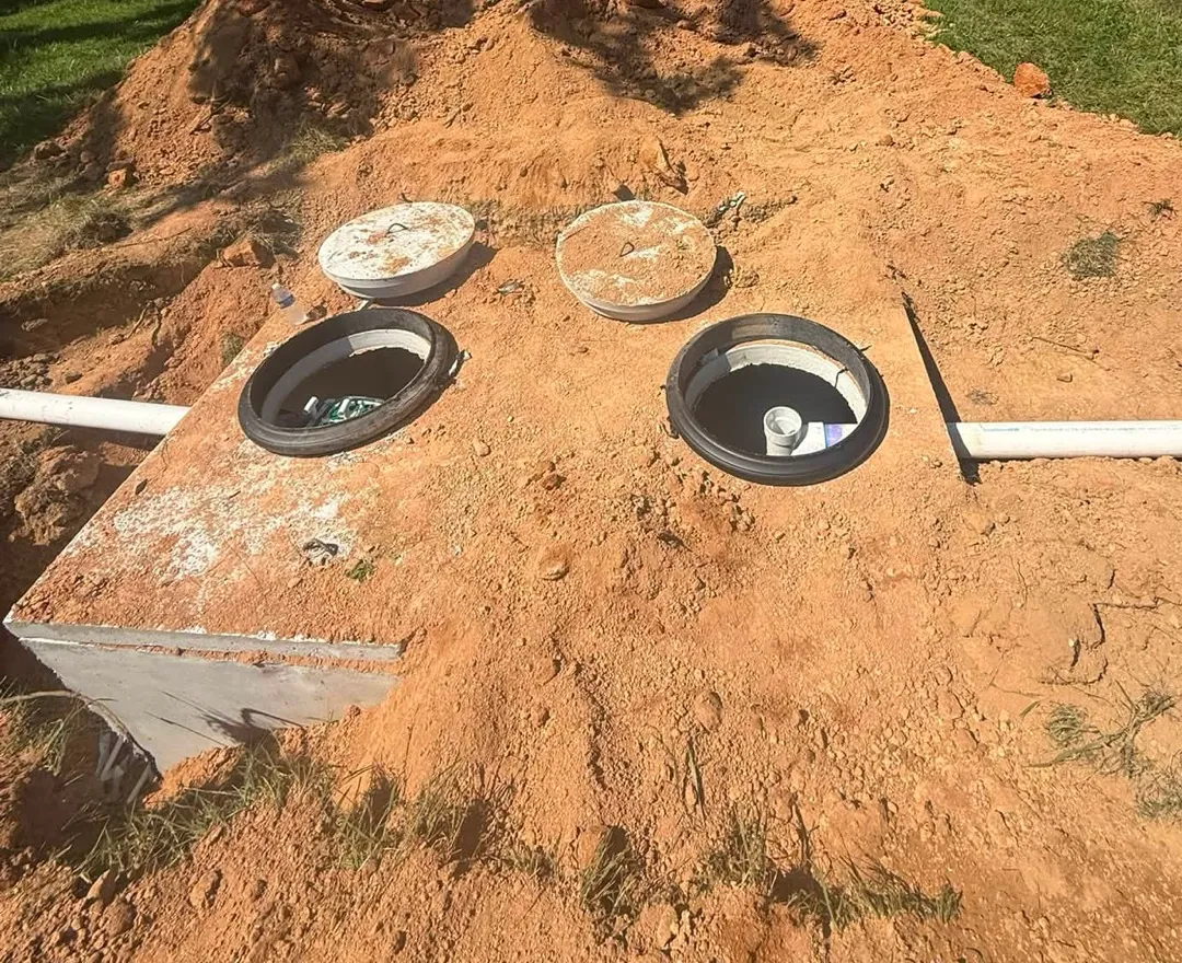 Concrete septic tank top with both access lids off and PVC pipes running in and out