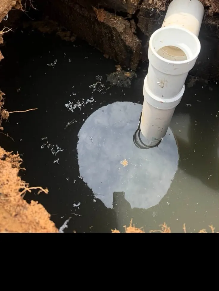 Top of a buried septic tank exposed at the bottom of a deep dig with a white PVC pipe standing up