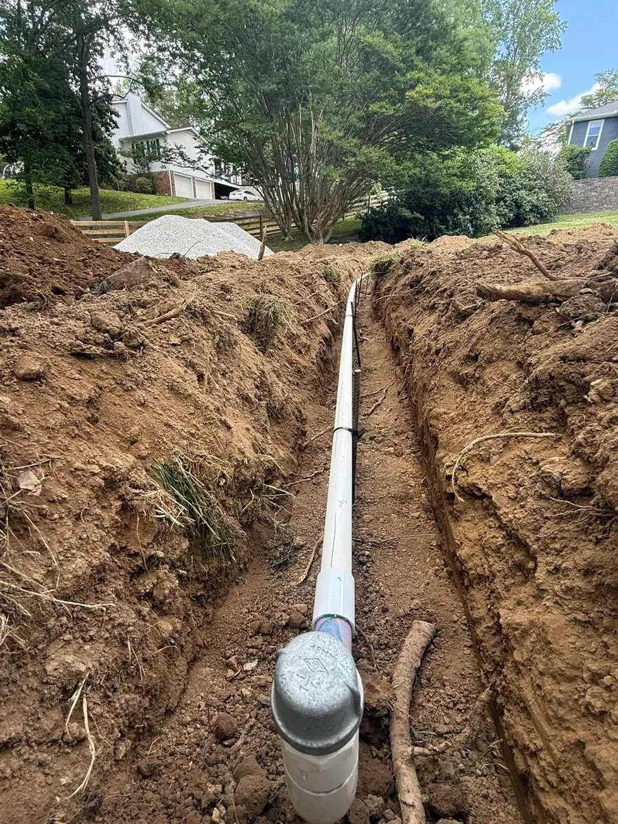 New PVC sewer line laid in an open trench and ending at a cleanout cap, with homes behind the dig